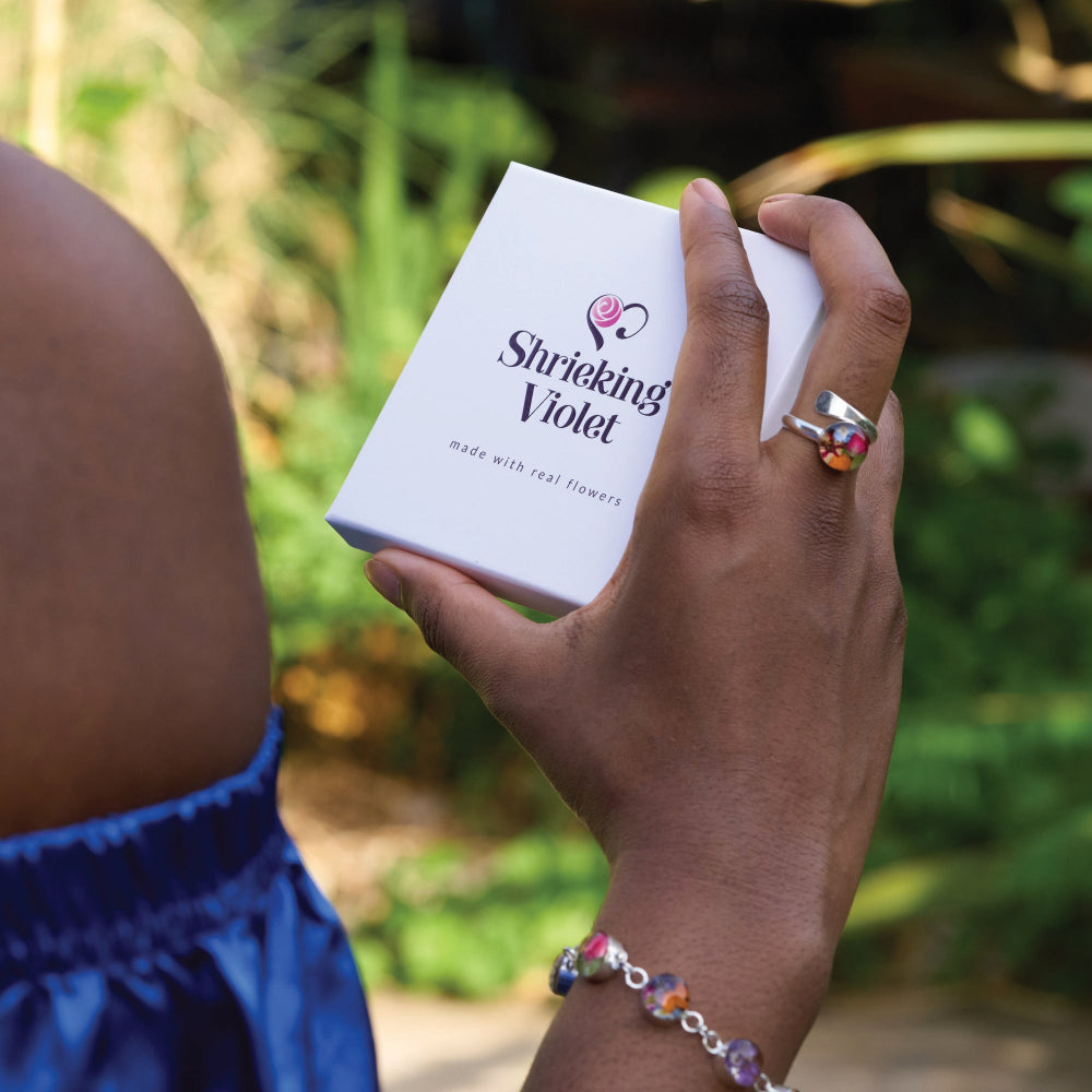Hand holding a 'Shrieking Violet' product box with a blurred green background